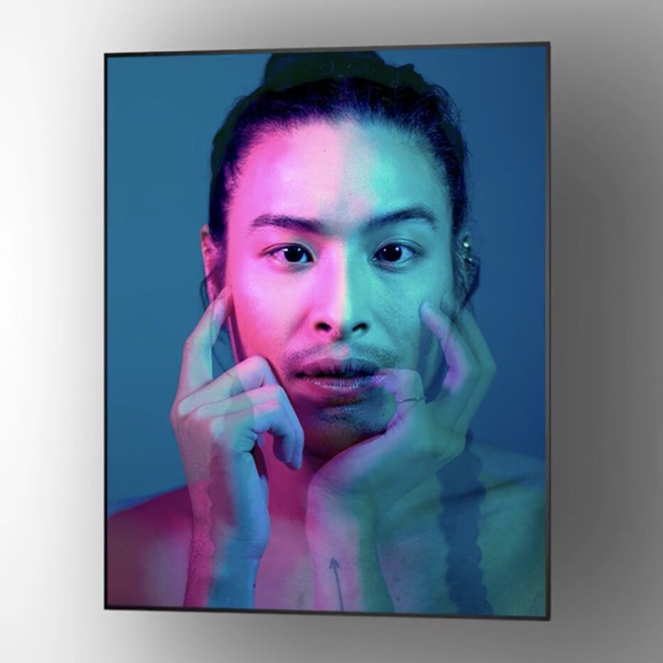 A portrait of a person with long hair in a bun, gazing forward. The image features a double exposure effect in pink and blue tones, showing two overlapping faces and hands against a neutral background.