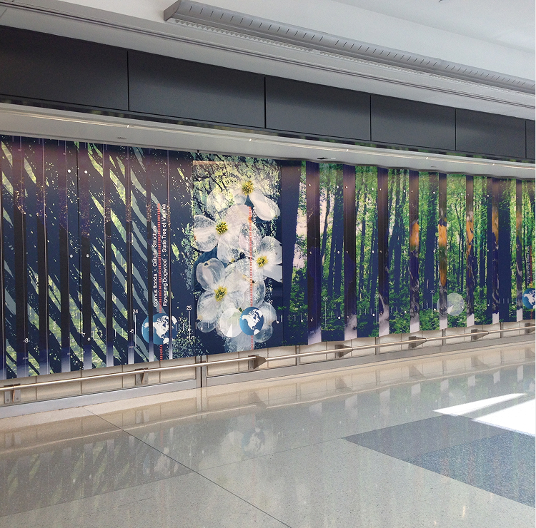Large wall mural in a modern indoor space featuring abstract art: white flowers in the center and vertical green lines resembling trees, blending natural elements with geometric patterns. Shiny floor reflects part of the mural.