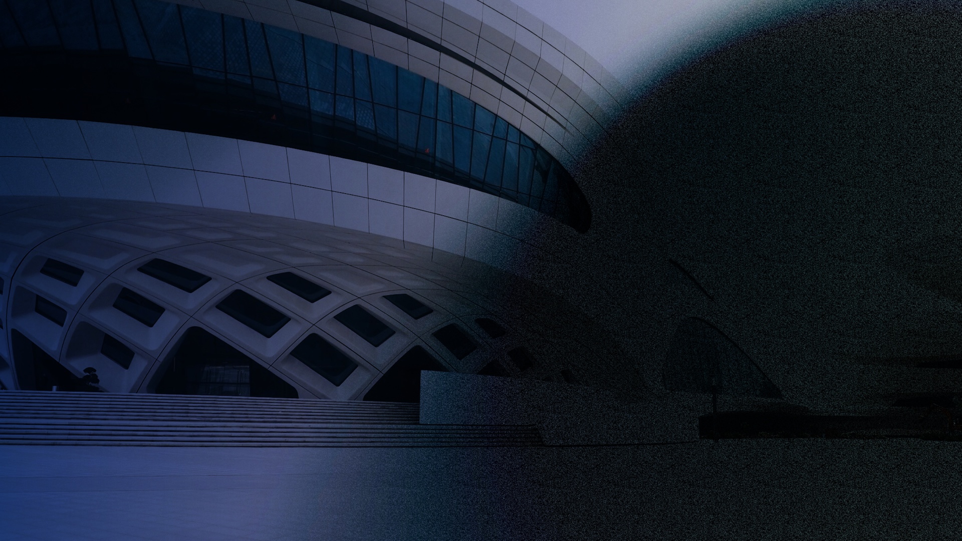 A modern building with curved, geometric architecture and large glass windows is partially obscured by a dark shadow, creating a dramatic contrast. Steps lead up to the structure’s entrance on the left.